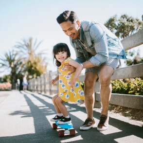 Asian father teaches his young daughter how to skateboard