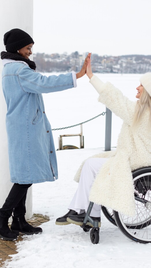 two women high-fiving and smiling at each other bundled up outside in the snow