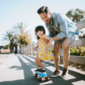 Asian father teaches his young daughter how to skateboard