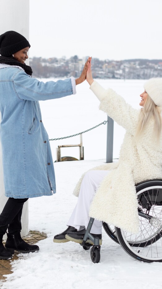 two women high-fiving and smiling at each other bundled up outside in the snow