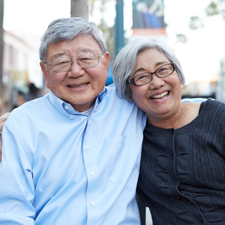 Older Asian couple sitting on a bench smiling